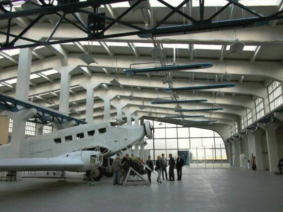 Flugzeughalle mit historischem Flugzeug und Besuchern.