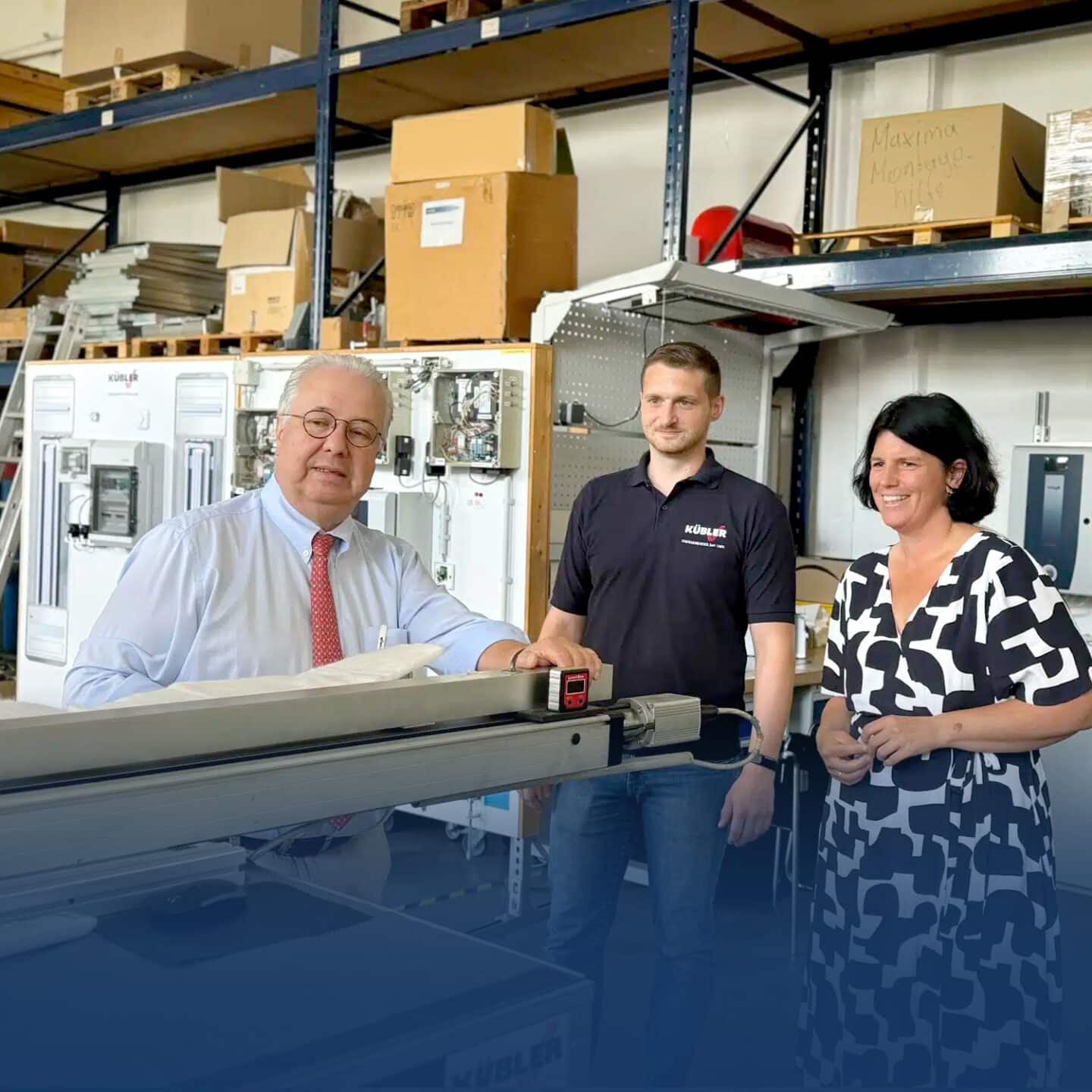 Three people are standing in an industrial warehouse.