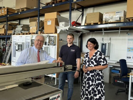 Three people are standing in an industrial hall.